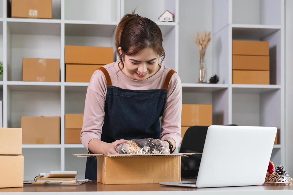 A small business owner packing orders beside a laptop